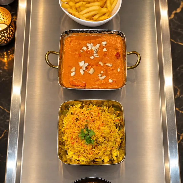 A creamy curry topped with cashews, pilau rice, a karahi curry and chips served on a tray