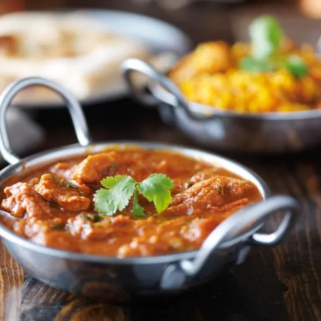 A karahi curry in a cast iron wok, served with naan and rice