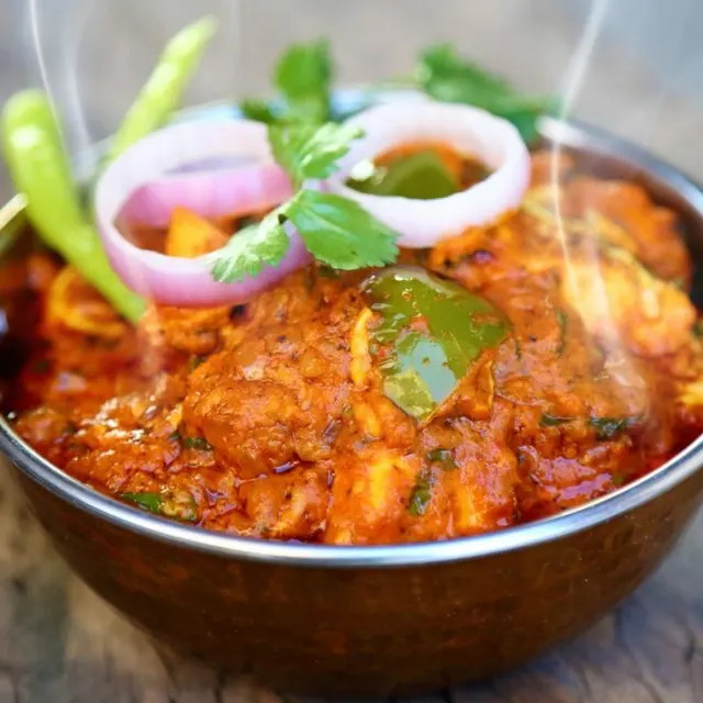 A steaming karahi curry topped with fresh onion and chilli