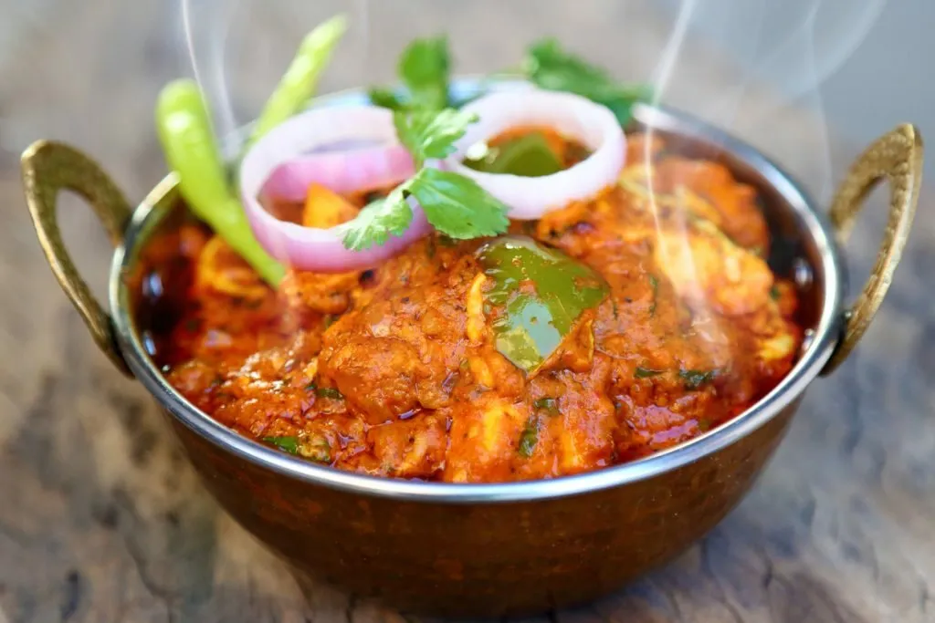 A steaming karahi curry garnished with fresh onion, coriander and chilli