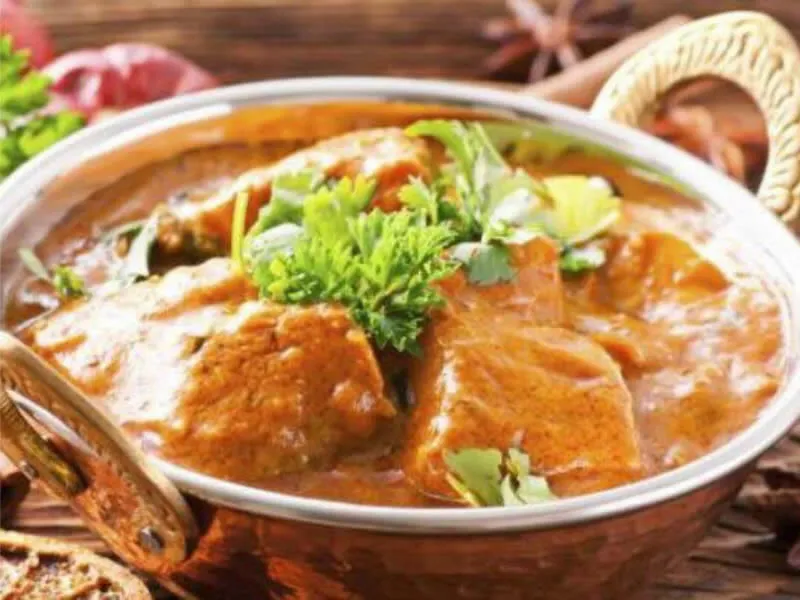 A lamb curry served in a copper bowl with a basket of naan