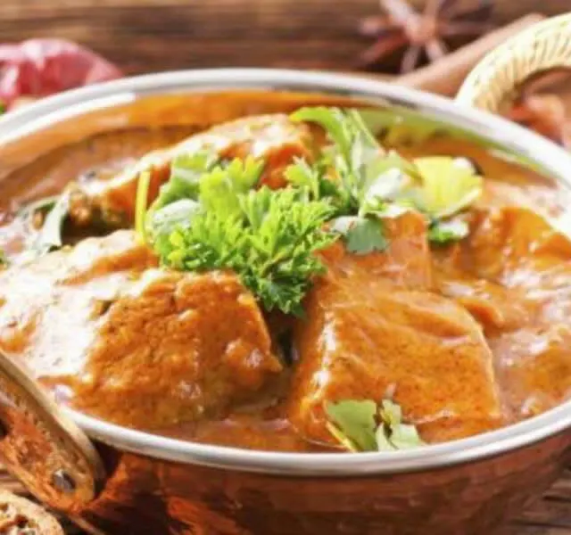 A lamb curry served in a copper bowl with a basket of naan